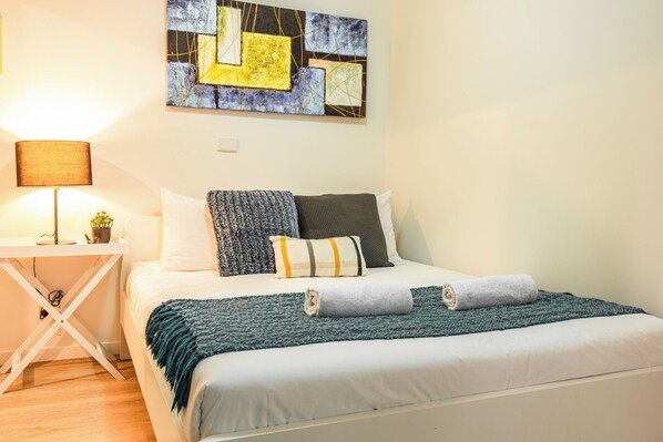 Relax in a serene bedroom with a comfortable bed, a potted plant, and a unique abstract art piece above.