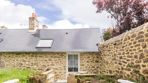 A stone house with a wooden deck, a small table, and two white chairs.