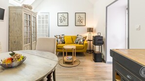 A modern living room with a high ceiling, a yellow sofa, a wooden cabinet, and a dining table with a fruit bowl.