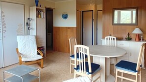 A compact room with a round table, two chairs, a bookshelf, and a door leading to another room. - Seaside Retreat: Cozy 1BR Apt Steps from Beach & Shops (Seignosse)