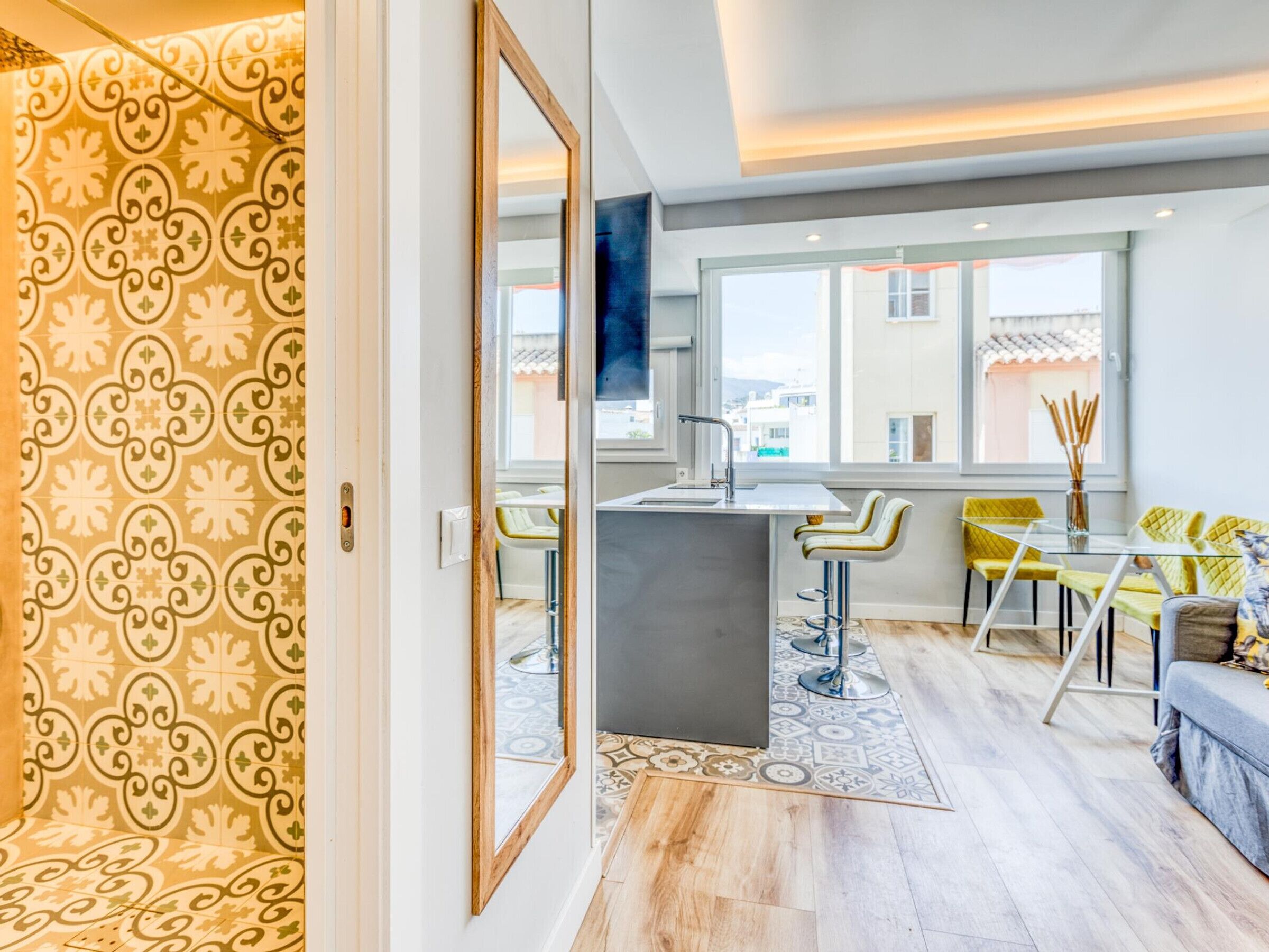 Ein modernes Wohnzimmer mit Küchenbereich, großen Fenstern und ornamentalem Wandpapier.