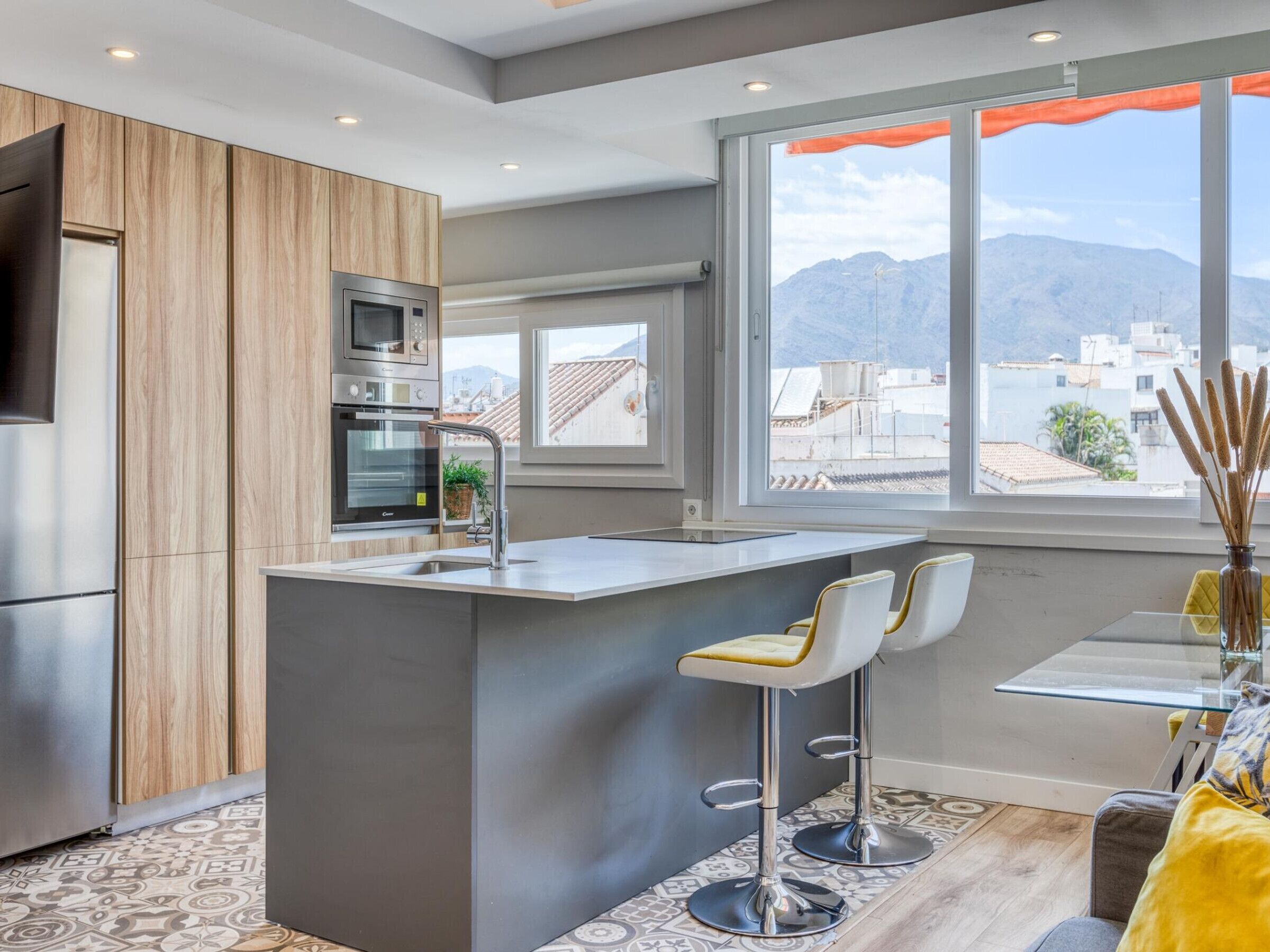 Een moderne keuken met inbouwapparatuur, een centraal eiland met barstoelen en een groot raam met uitzicht op de stad en de bergen.