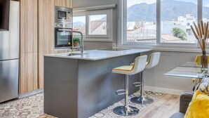 A modern kitchen with built-in appliances, a central island with bar stools, and a large window offering a view of the city and mountains. - Modern renovated apartment near beach, 1 bedroom (Estepona)