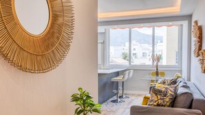 A modern living room with a large window, a round mirror, a plant, and a sofa with cushions. - Modern renovated apartment near beach, 1 bedroom (Estepona)
