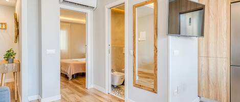 A modern hotel room with a wooden floor, a bed, a bathroom with a bathtub, and a TV mounted on the wall.