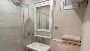 Un baño con cabina de ducha de vidrio, lavamanos blanco, espejo, inodoro y azulejos de suelo con diseño.