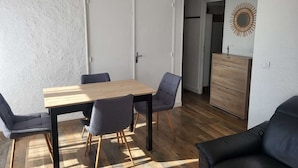 Een moderne woonkamer met een houten eettafel, vier stoelen, een zwarte leren bank en een houten dressoir.