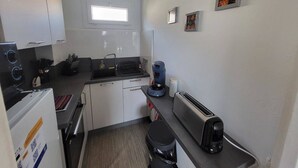 Een compacte keuken met witte kastjes, een inbouwoven, een koffiezetapparaat en een broodrooster.