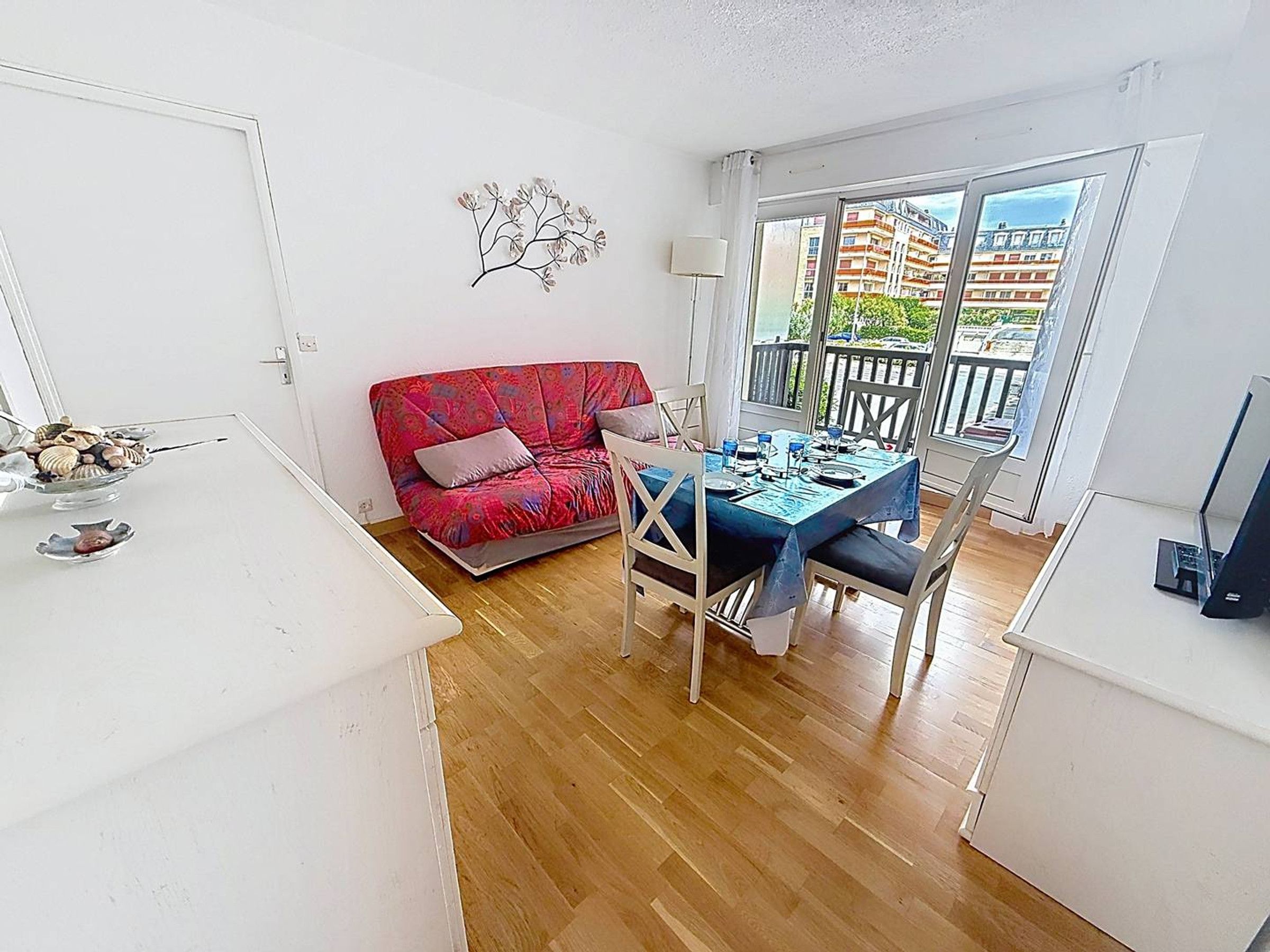A room with a dining table set for four, a red sofa, a white armchair, and a decorative plant on the wall.