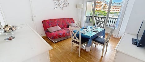 A room with a dining table set for four, a red sofa, a white armchair, and a decorative plant on the wall.
