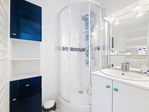 Un baño moderno con cabina de ducha de vidrio, un lavabo blanco con espejo y un reverso de azulejos.
