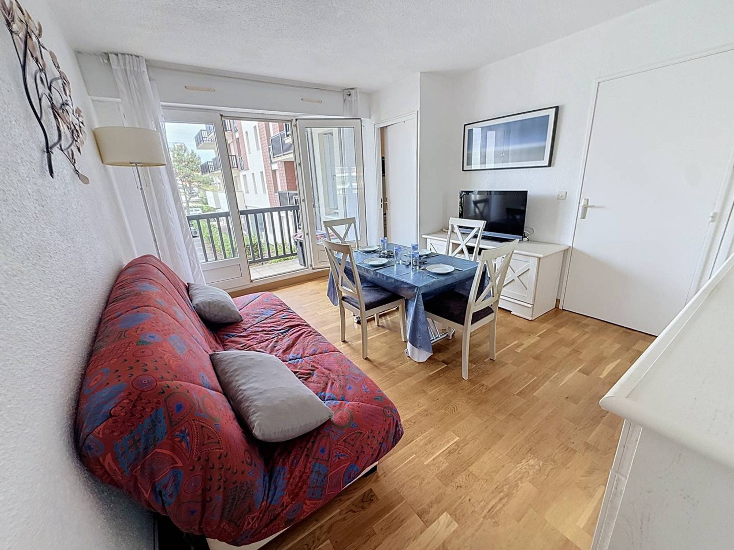 Ein Wohnzimmer mit einer Couch, einem Esstisch, Stühlen, einem Fernseher und einem Balkon mit Blick.