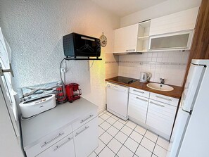 A compact kitchen with white cabinets, a microwave, a coffee maker, and a dishwasher.