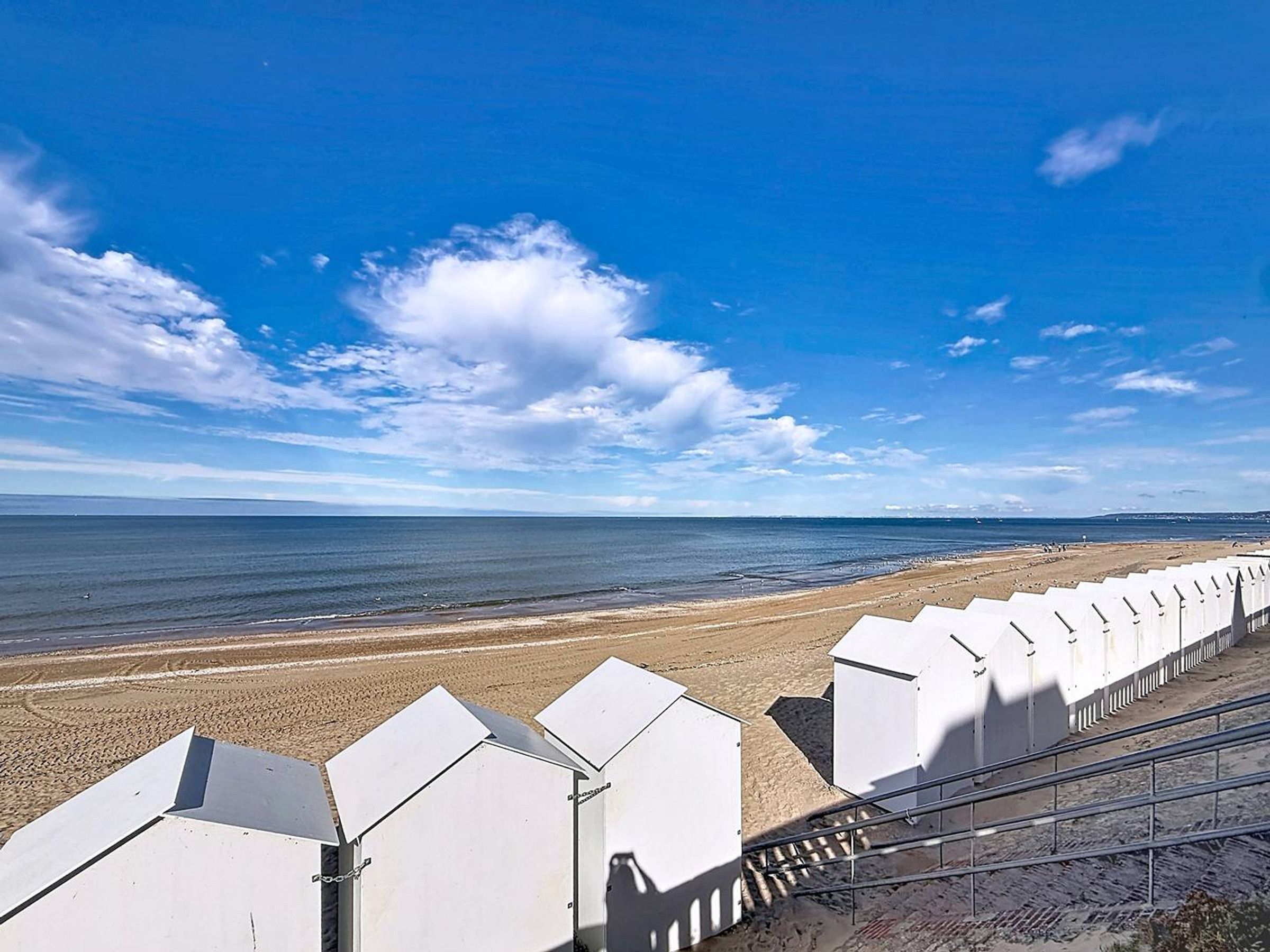 Een strand met een rij witte strandhutten en een helderblauwe lucht.