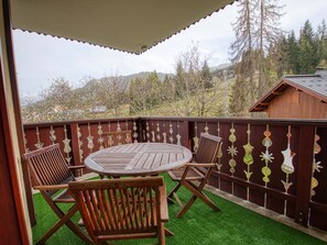 Een overdekt terras met een ronde tafel en stoelen, omgeven door een decoratieve omheining met hangende decoraties.