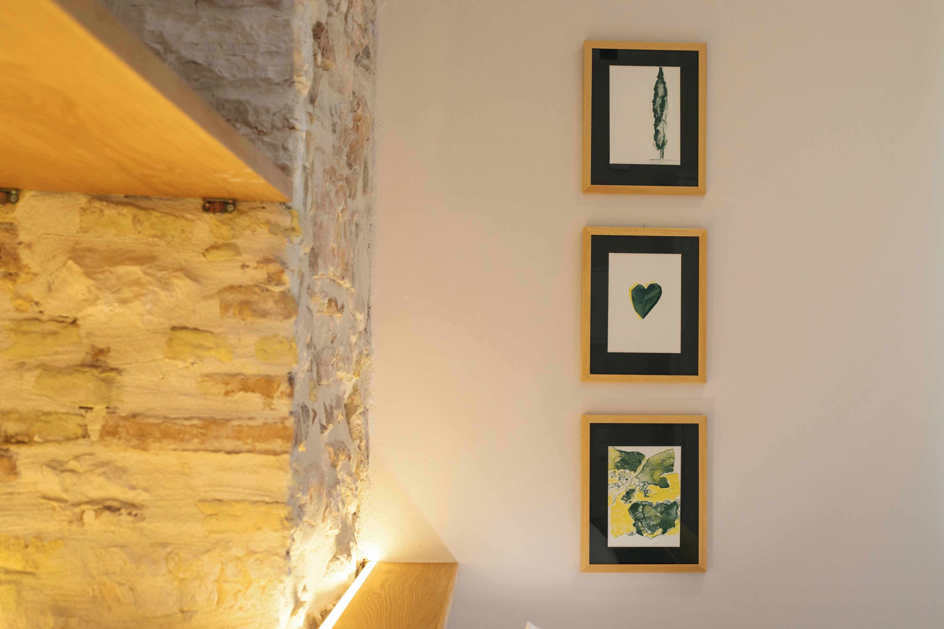 A room with a stone wall, a wooden beam, and three framed artworks on the wall.
