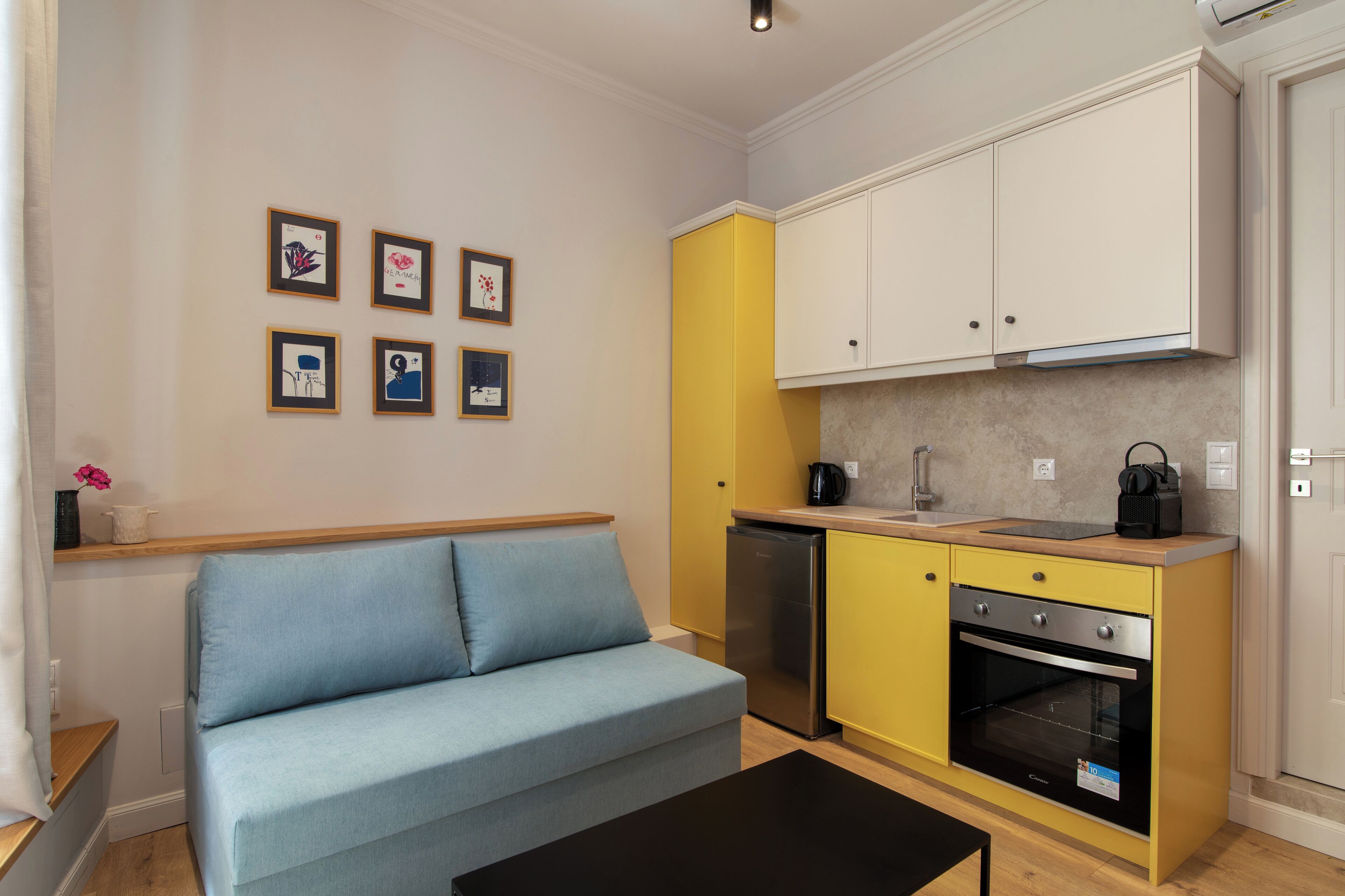 A compact living space with a sofa, kitchenette, and wall-mounted artwork.
