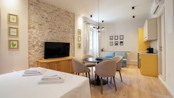 Una habitación de hotel moderna con una pared de piedra, un televisor de pantalla plana, un área de comedor con una mesa redonda y sillas, y una kitchenette.