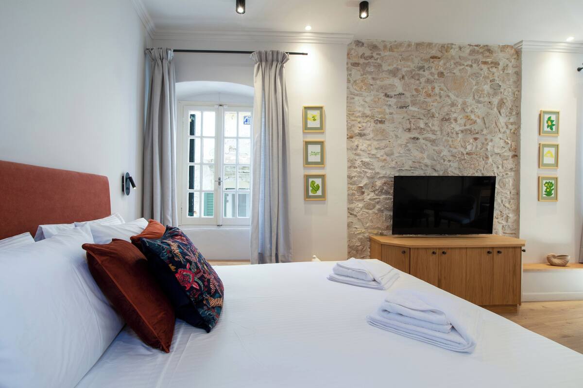 A bedroom with a bed, pillows, a TV on a wooden cabinet, and a stone wall.