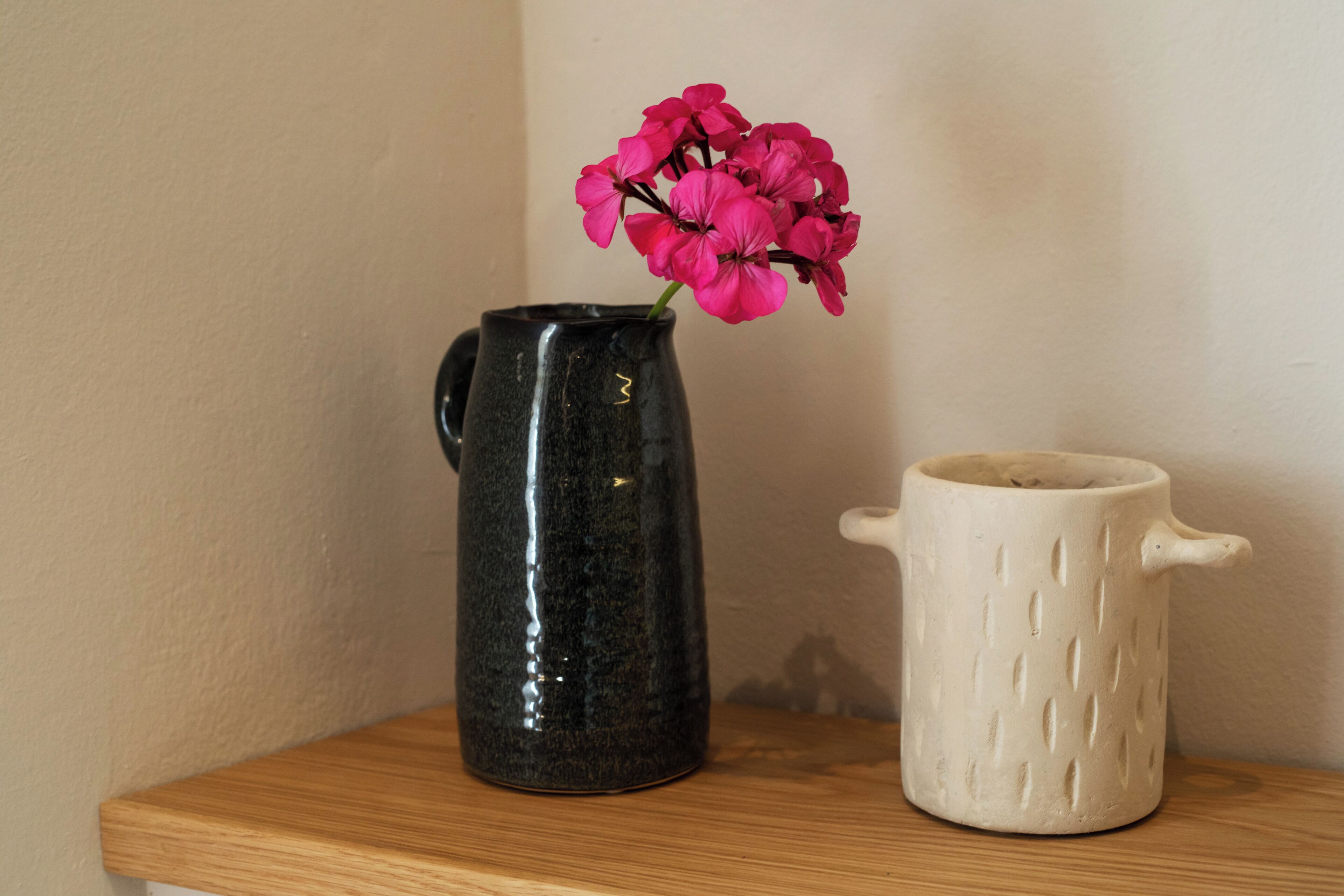 A black ceramic pitcher with a handle and a white ceramic mug with a handle on a wooden shelf.