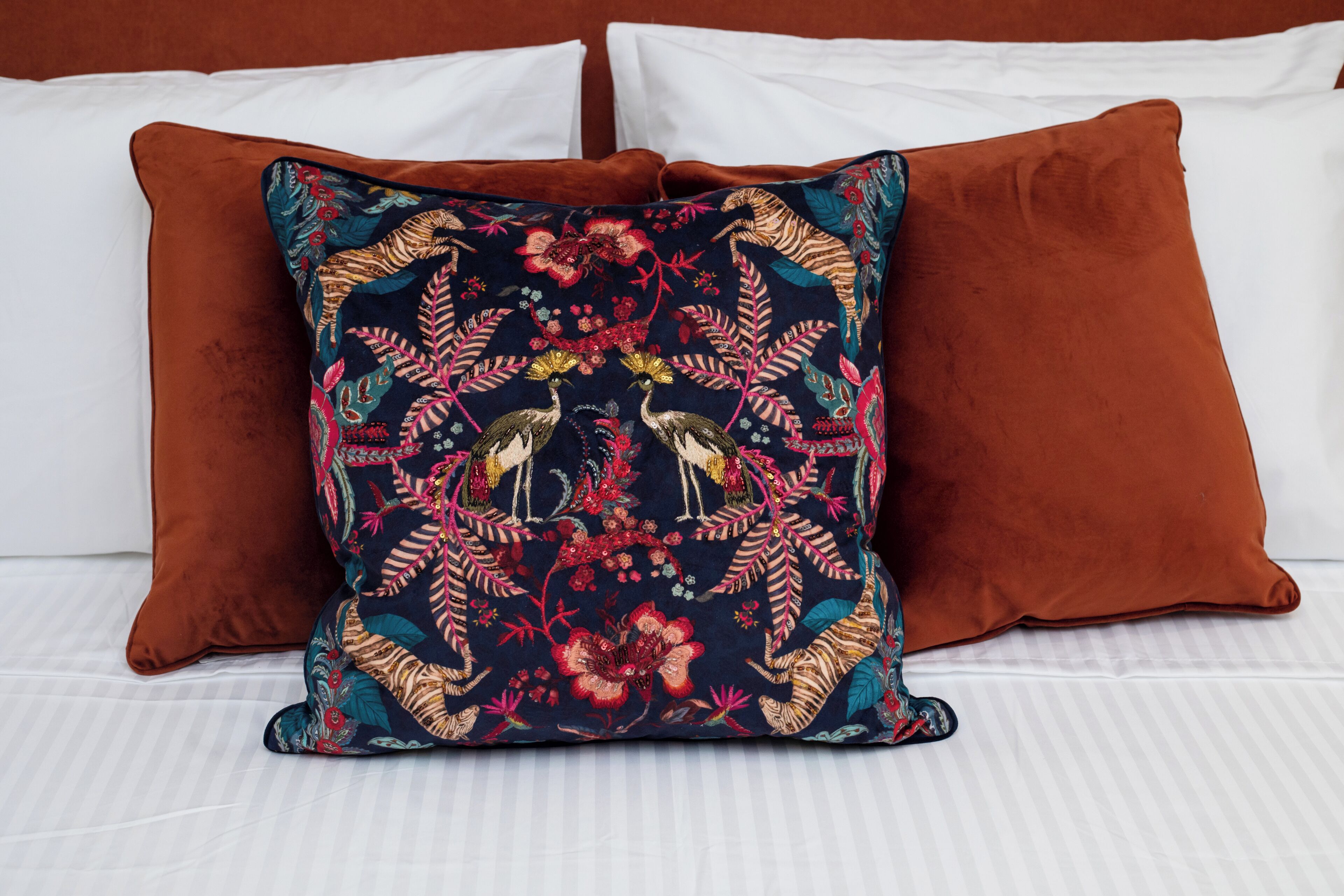 A bed with a patterned pillow and two solid-colored pillows.