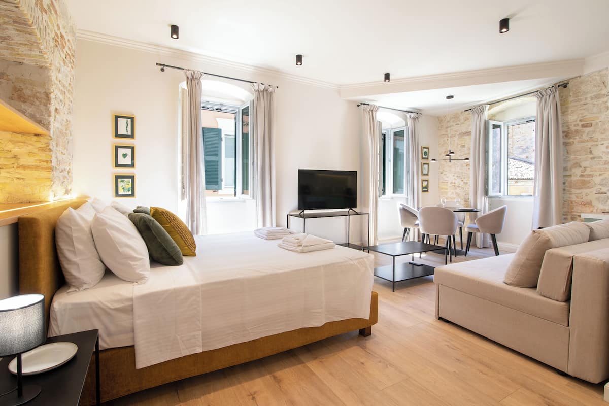 A modern hotel room with a large bed, a sofa, a TV, and a dining area.