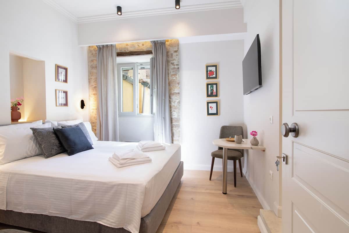 A bedroom with a bed, a desk, a chair, a TV, and a window with curtains.