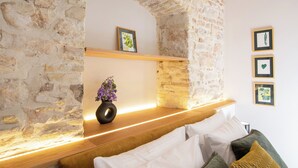 Une pièce chaleureuse avec un mur en pierre, une étagère en bois ornée d’un vase de fleurs et des tableaux encadrés accrochés au mur.