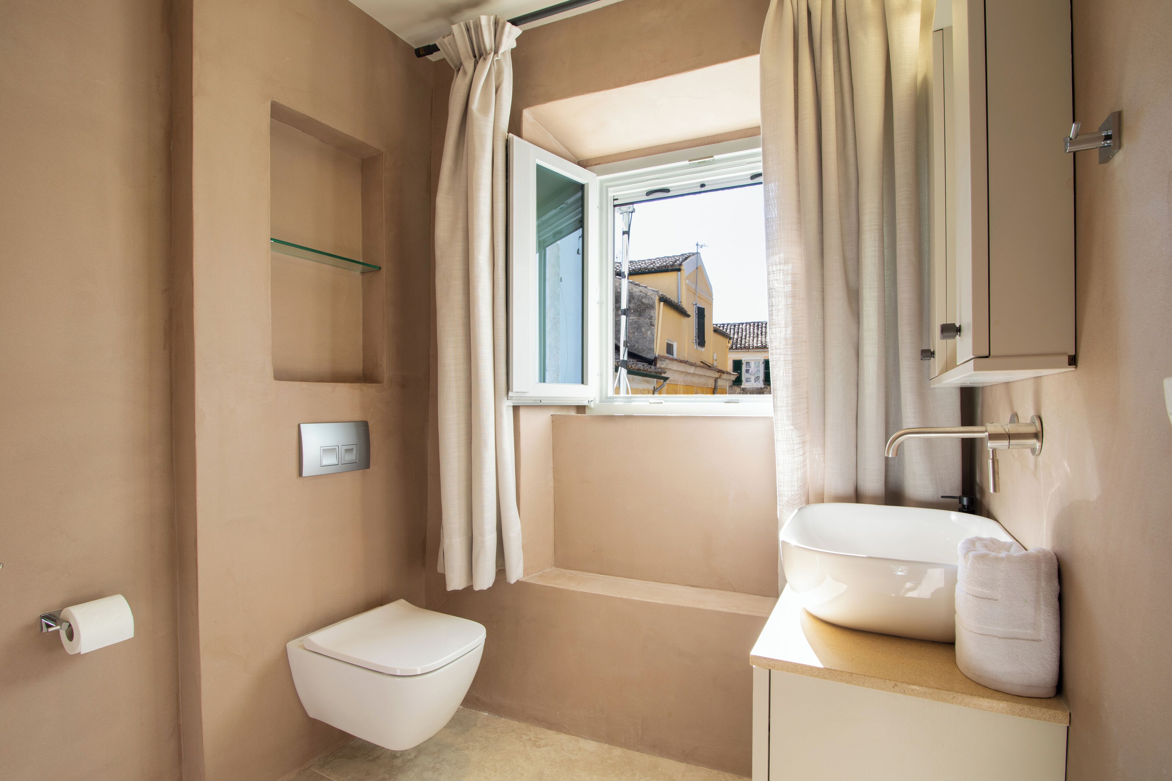 A bathroom with a toilet, sink, and window with curtains.