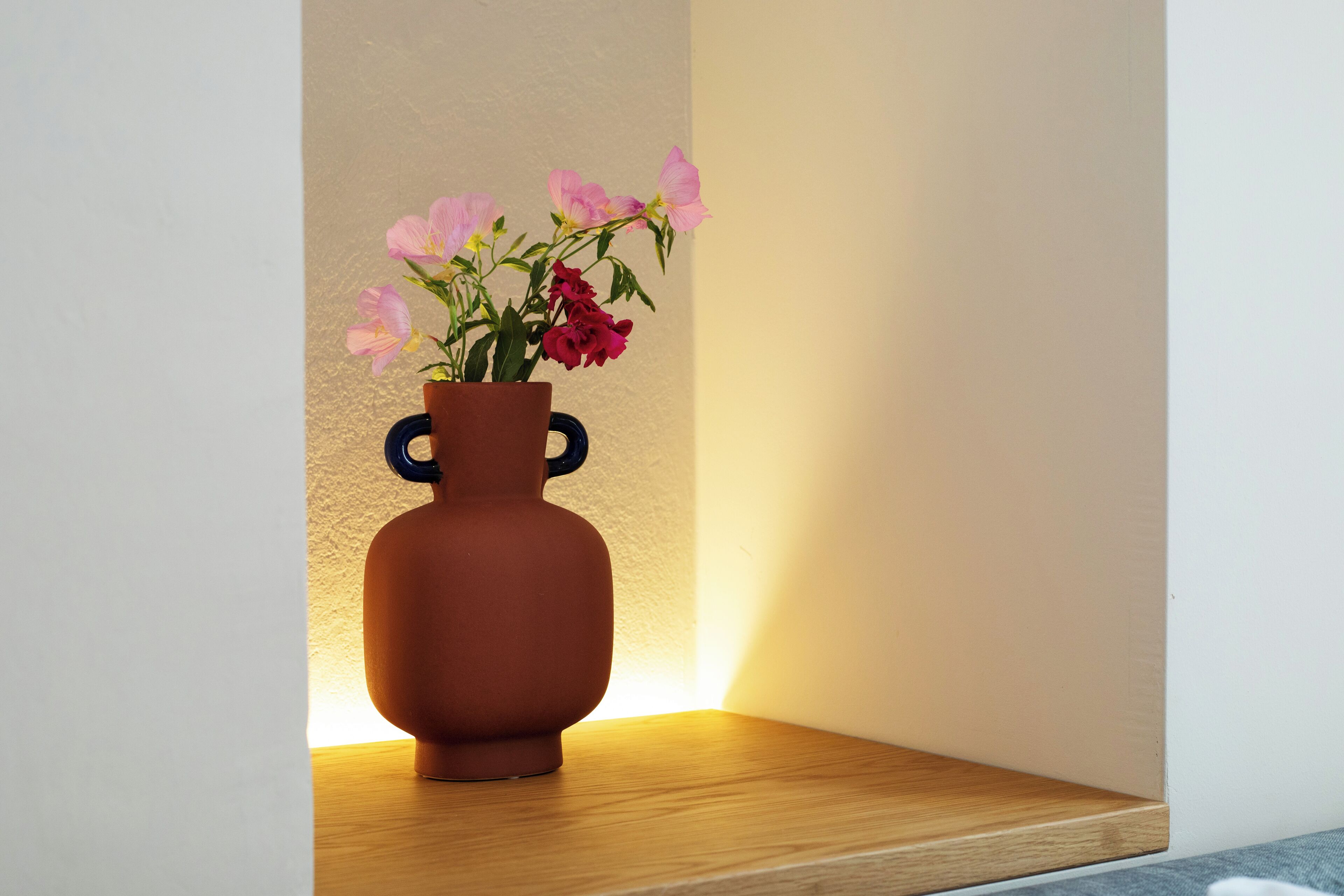 Een terracotta vaas met oren op een houten plank tegen een muur.