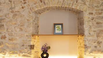 Una stanza con pareti in pietra, una panca di legno, un vaso con fiori e un quadro appeso al muro.