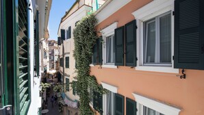 Une rue étroite bordée d’immeubles aux volets verts et d’un mur recouvert de lierre.