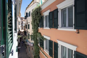 Ένας στενός δρόμος με κτίρια που διαθέτουν πράσινα παντζούρια και έναν τοίχο καλυμμένο με αναρριχώμενα φυτά.