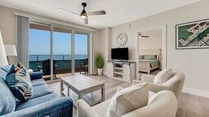 Ein modernes Wohnzimmer mit großem Fernseher, Deckenventilator, Esstisch und einer Couch.