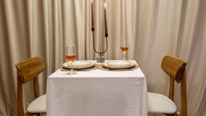 Une table dressée pour deux personnes, recouverte d’une nappe blanche, avec deux chaises en bois, un chandelier avec des bougies et un verre de vin.