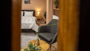 Une chambre d’hôtel avec un lit, une table de chevet, une lampe, une chaise et une petite table sur laquelle est posée une plante.