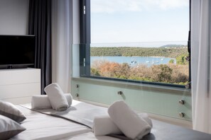 Ein Hotelzimmer mit Bett, Fernseher und Fenster mit Blick auf einen Jachthafen und Hügel.