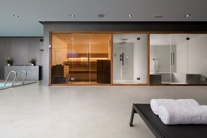 Ein moderner Wellnessraum mit einer gläsernen Duschkabine, einer Holzbank und einem Massagetisch mit Handtüchern.