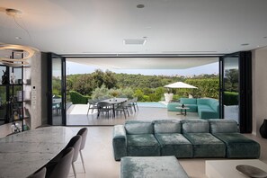 Ein modernes Wohnzimmer mit Essbereich, einer Couch und Blick auf einen Pool und Grünflächen.