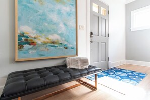 Una habitación con un banco de cuero negro, un cuadro abstracto grande, una puerta blanca y una alfombra azul estampada.
