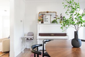 Een eethoek met een ronde tafel, een kinderstoel, een piano en een decoratief bord.