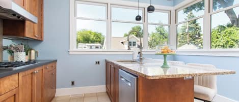 A kitchen with wooden cabinets, a granite countertop, a built-in dishwasher, and a window with a view of the neighborhood.