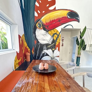 A dining table with a tropical mural, a potted plant, and a modern cabinet.