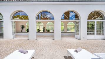 A spa area with three arched windows, a tiled floor, and two lounge chairs with towels.