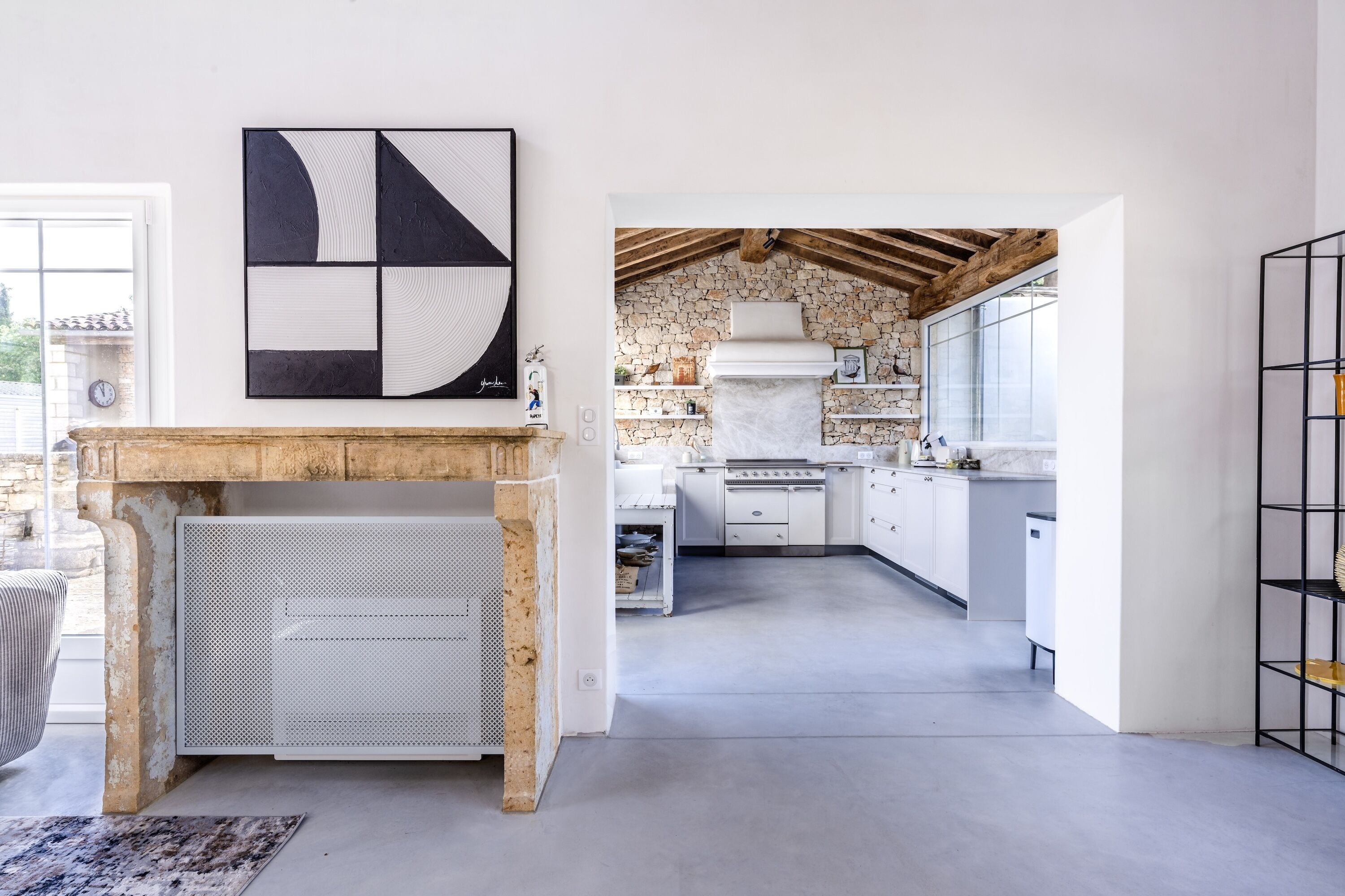 A modern kitchen with a stone wall, white cabinetry, and a large window.