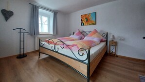 A bedroom with a bed, a window with curtains, a radiator, a wall-mounted picture, and a small bedside table with a lamp. - Feel-good place in the heart of Pfaffenwinkel:Freshly renovated with its own terrace (Rottenbuch)
