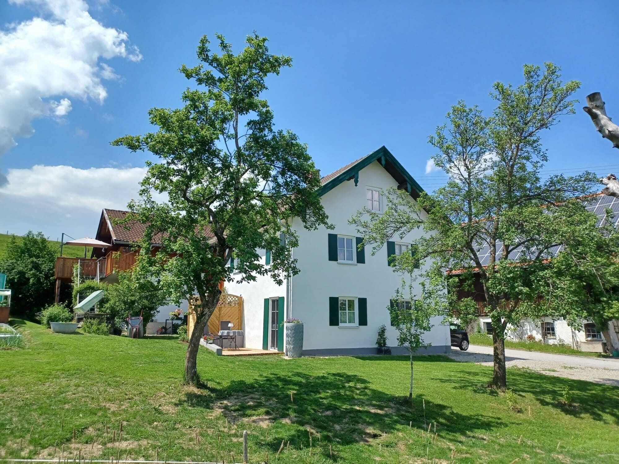 Ein zweistöckiges Haus mit einem grünen Dach, weißen Wänden und einer kleinen Veranda.