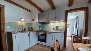 A compact kitchen with white cabinets, a built-in oven, a coffee maker, and a dining area with a wooden table and chairs. - Feel-good place in the heart of Pfaffenwinkel:Freshly renovated with its own terrace (Rottenbuch)