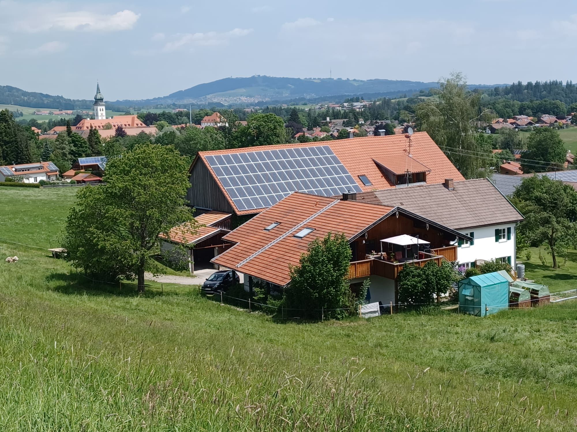 Une maison de campagne dotée de panneaux solaires, entourée de verdure et surplombant une église située au loin.