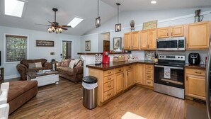 A spacious living area with a sofa set, a coffee table, and a trash can. The kitchen features wooden cabinets, a microwave, and an oven. - Cozy Nest Cabin at Coosawattee (Ellijay)